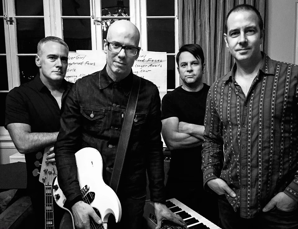 A black and white photo of the progressive pop band Plastic Ants in their rehearsal space and with their instruments, featuring band members John Curley, Robert Cherry, Joe Klug and Guy Vanasse. 
